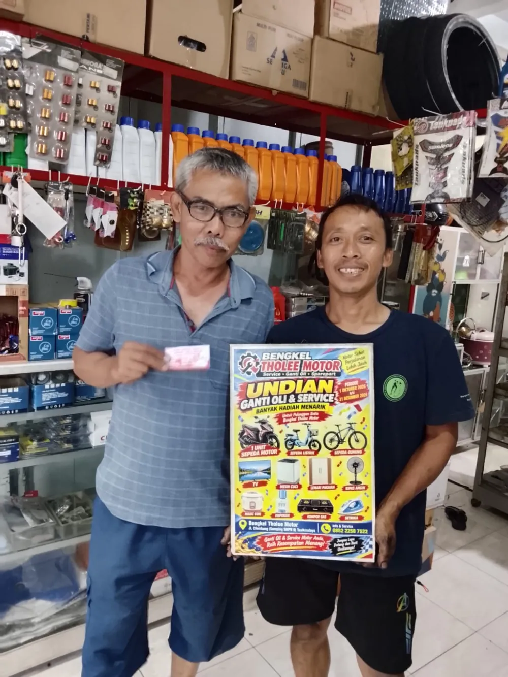 Pelanggan memegang kupon dan poster undian di depan rak oli